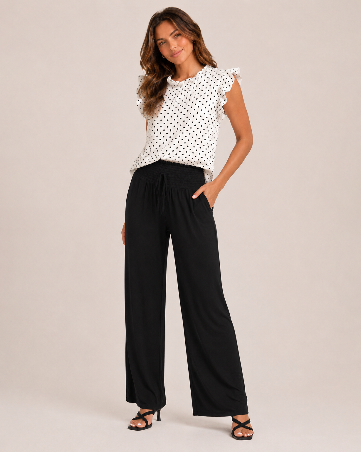 Side view of woman wearing black smocked wide-leg pants and a white sleeveless top on a beige background