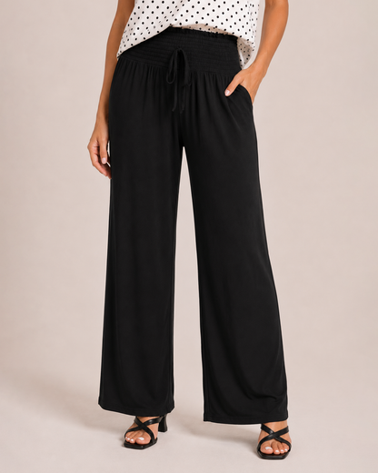 Close-up of woman wearing black smocked wide-leg pants with a drawstring waist and side pockets on a beige background