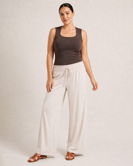 Woman wearing cream smocked wide-leg pants and a brown sleeveless top on a beige background