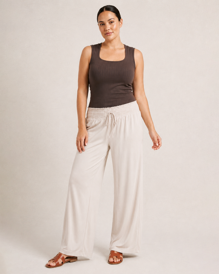 Woman wearing cream smocked wide-leg pants and a brown sleeveless top on a beige background
