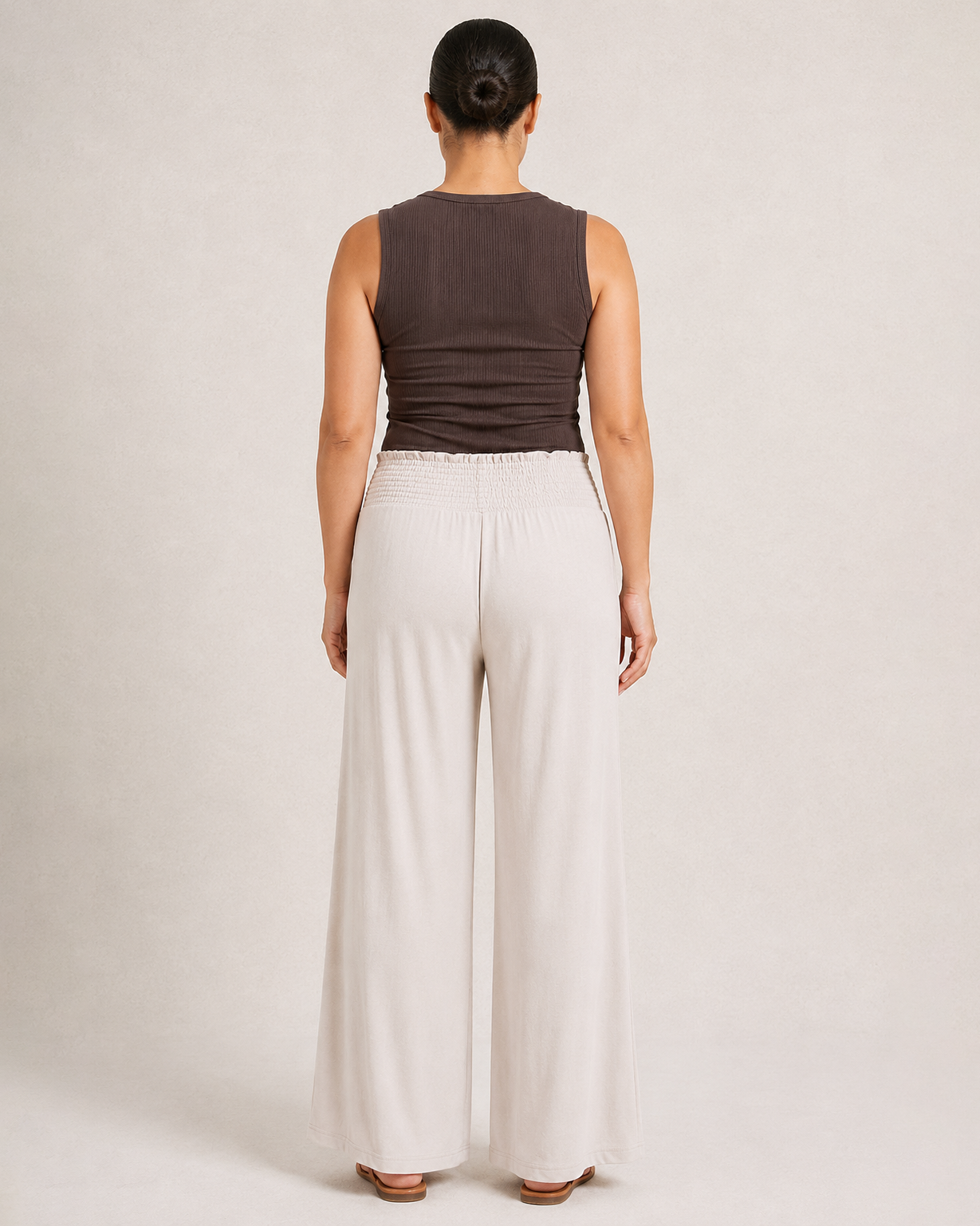 Back view of woman wearing cream smocked wide-leg pants and a brown sleeveless top on a beige background