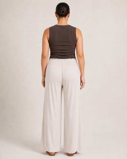 Back view of woman wearing cream smocked wide-leg pants and a brown sleeveless top on a beige background