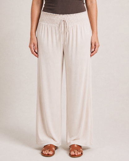 Close-up of cream smocked wide-leg pants with a drawstring waist on a beige background