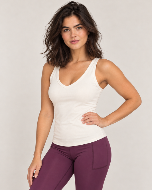 A woman modeling a fitted white sculpt bra tank top paired with purple leggings, standing against a light gray studio background.