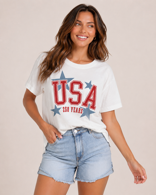 Woman wearing a white t-shirt with 'USA 250 Years' text and blue shorts on a beige background