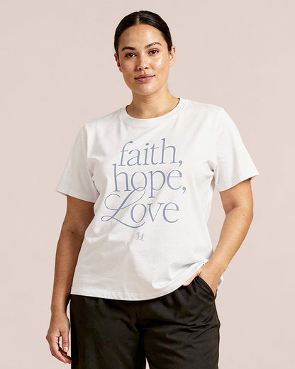 Model wearing a white t-shirt with 'faith, hope, love' text on a beige background