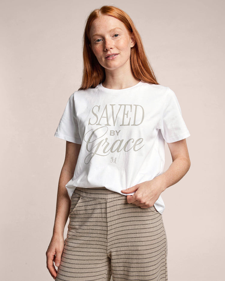 Person wearing a white t-shirt with 'Saved by Grace' text on a beige background
