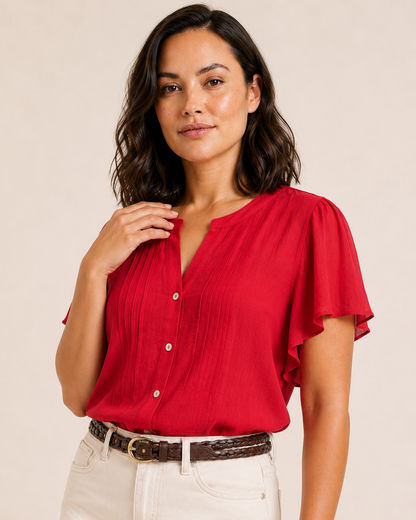 Close-up of a woman wearing a red flutter-sleeve blouse with pintuck details, button-front accents, and natural shorts on a beige background
