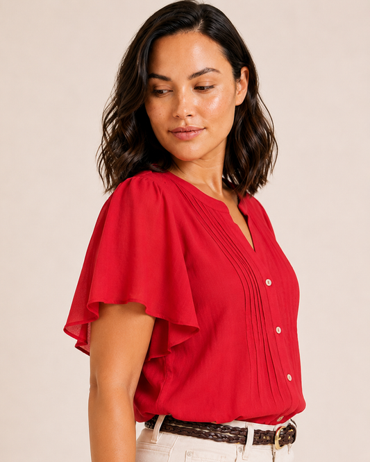 Close-up of a woman wearing a red flutter-sleeve blouse with pintuck details, button-front accents, and natural shorts on a beige background