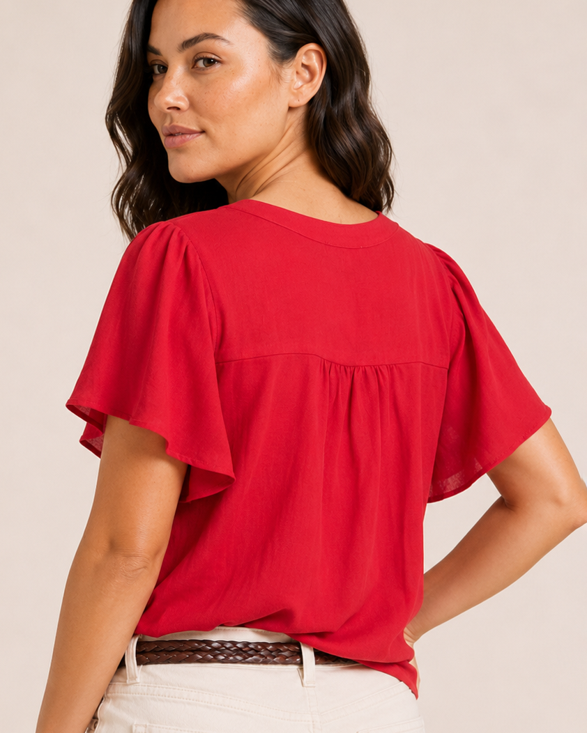 Back view of a woman wearing a red flutter-sleeve blouse and natural shorts on a beige background