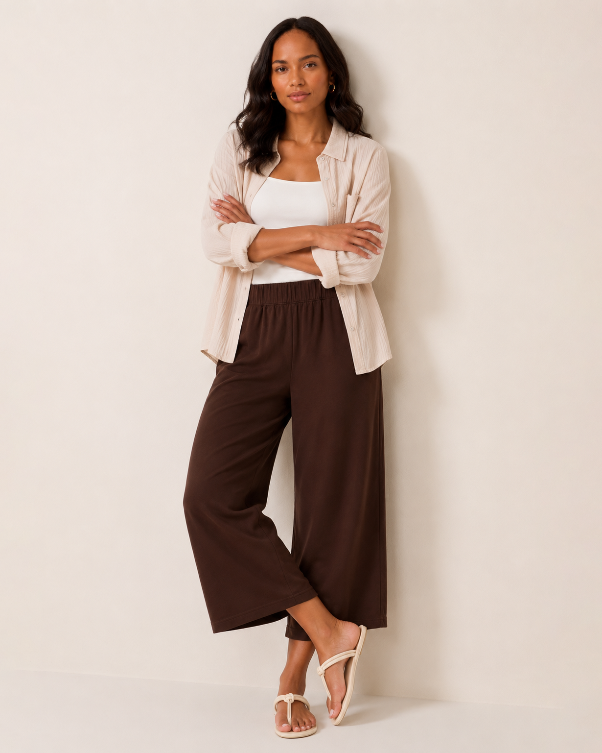 Woman wearing brown wide-leg pants, a white tank top, and a beige button-front shirt on a beige background