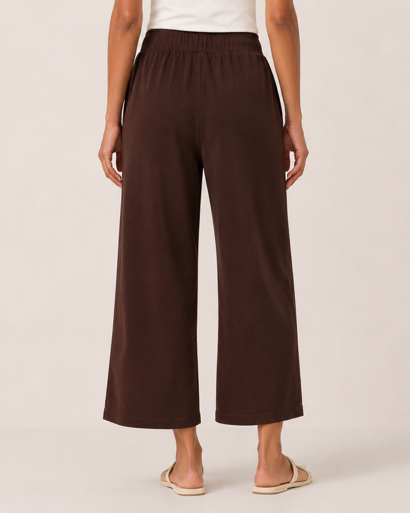 Back view of a woman wearing brown wide-leg pants and a white tank top on a beige background