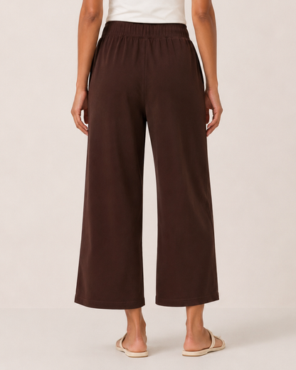 Back view of a woman wearing brown wide-leg pants and a white tank top on a beige background