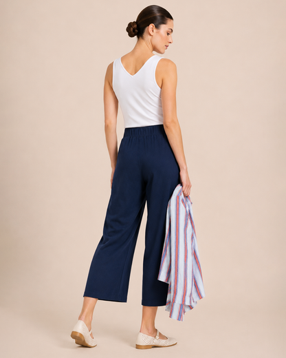 Back view of a woman wearing navy wide-leg pants and a white tank top on a beige background