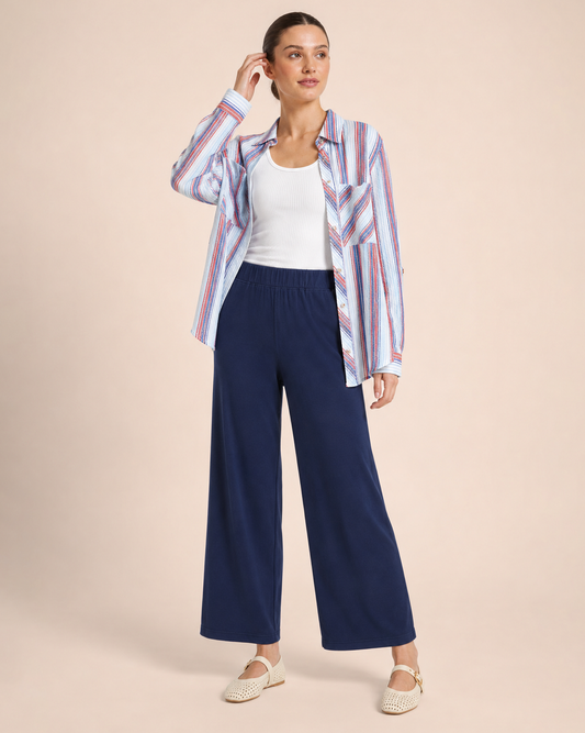 Woman wearing navy wide-leg pants, a white tank top, and a striped button-front shirt on a beige background