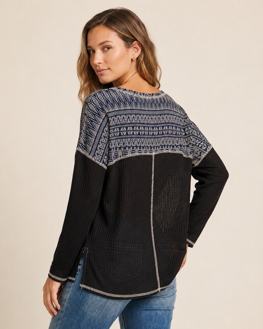 Cropped view of a woman wearing a black and gray color-block knit top with a contrasting patterned yoke on a beige background