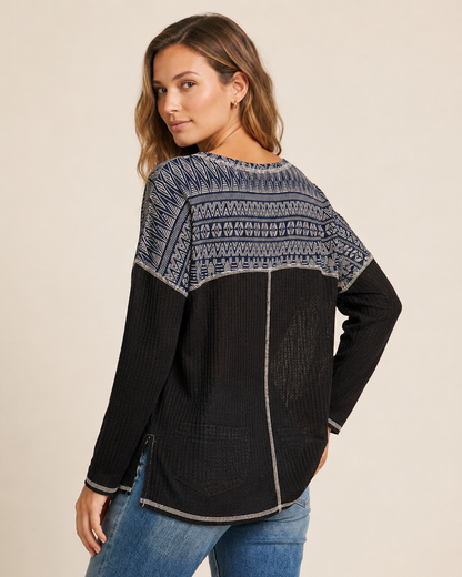 Cropped view of a woman wearing a black and gray color-block knit top with a contrasting patterned yoke on a beige background