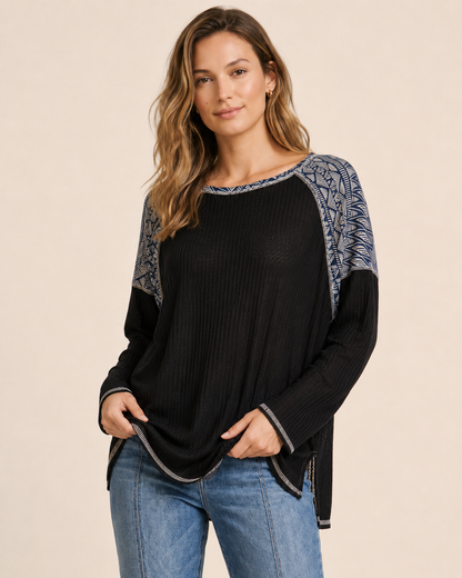 Front view of a woman wearing a black and gray color-block knit top with blue jeans on a beige background