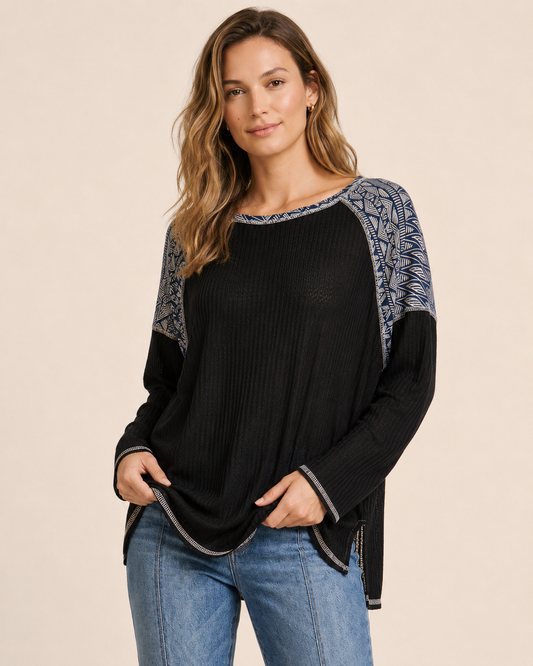 Front view of a woman wearing a black and gray color-block knit top with blue jeans on a beige background