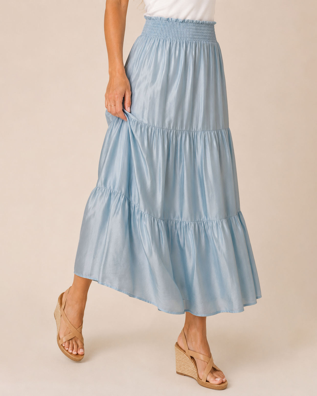 A light blue tiered maxi skirt with an elastic waistband, shown on a model wearing beige wedge sandals against a solid beige background.