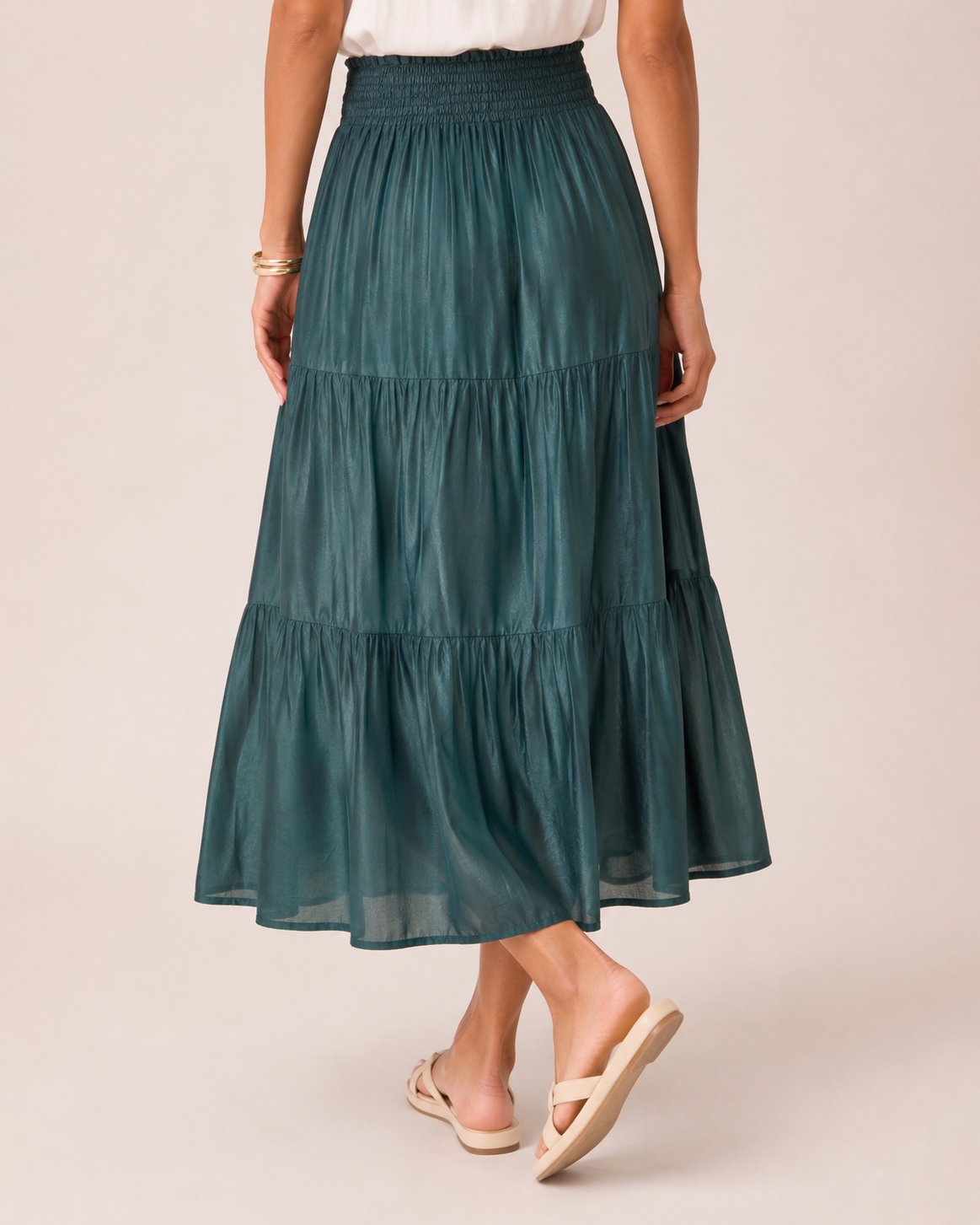 Close-up view of a woman wearing an ivy tiered maxi skirt and a white flutter sleeve blouse on a beige background