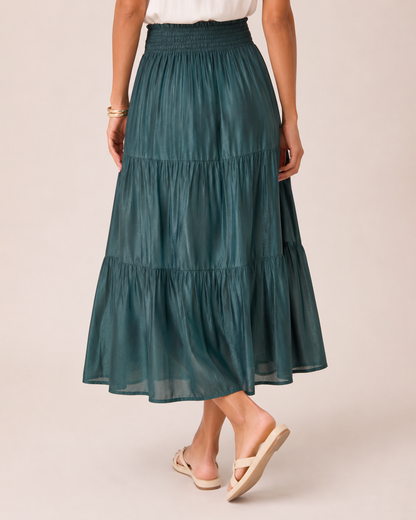 Close-up view of a woman wearing an ivy tiered maxi skirt and a white flutter sleeve blouse on a beige background