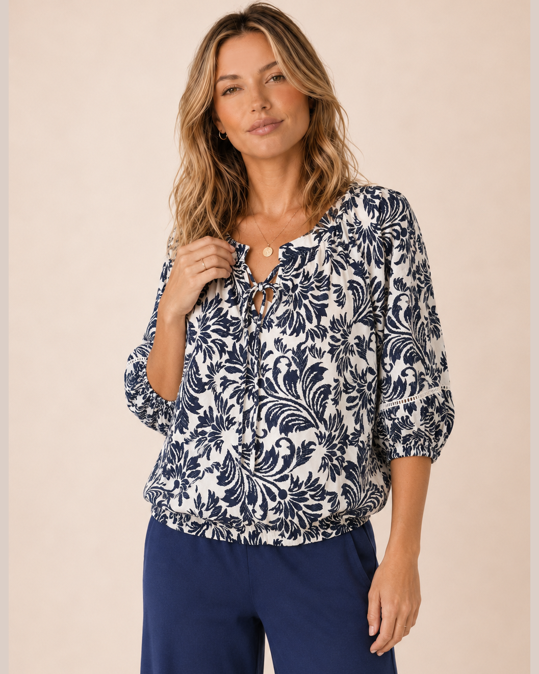 Front view of a woman wearing a white and navy floral peasant top and navy wide-leg pants on a beige background