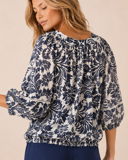 Back view of a woman wearing a white and navy floral peasant top on a beige background
