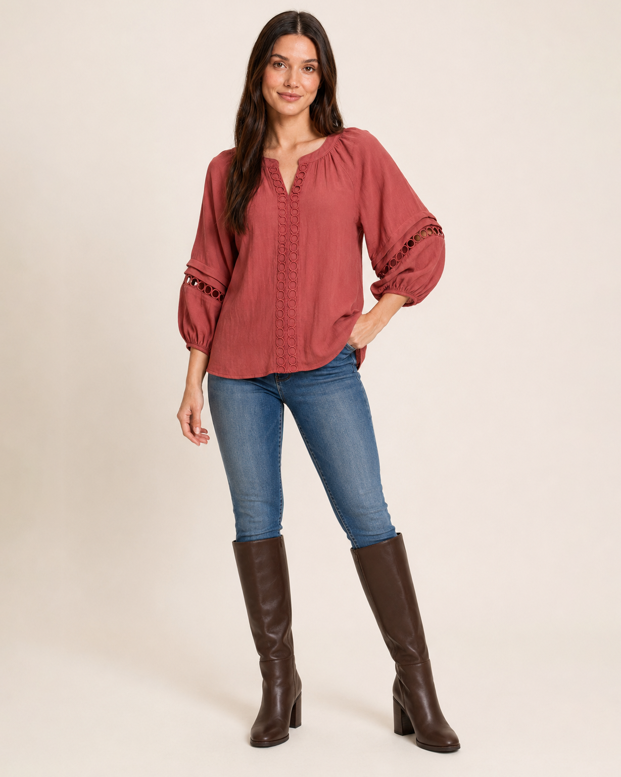 Woman wearing a warm rust-red textured knit top with balloon sleeves, blue jeans, and black boots on a beige background