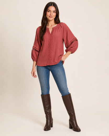 Woman wearing a warm rust-red textured knit top with balloon sleeves, blue jeans, and black boots on a beige background