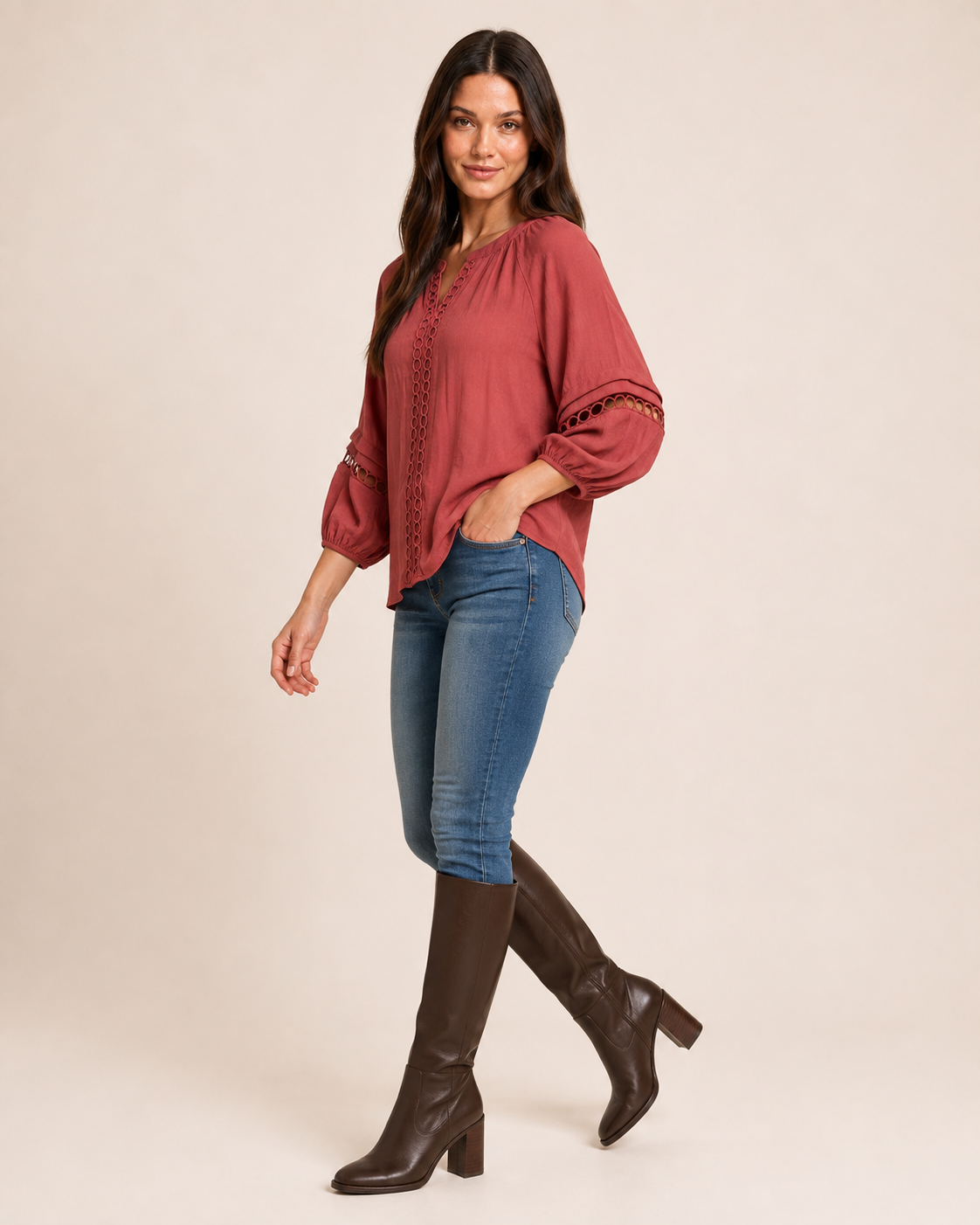 Side view of a woman wearing a warm rust-red textured knit top with balloon sleeves and blue jeans on a beige background