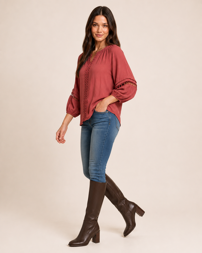Side view of a woman wearing a warm rust-red textured knit top with balloon sleeves and blue jeans on a beige background