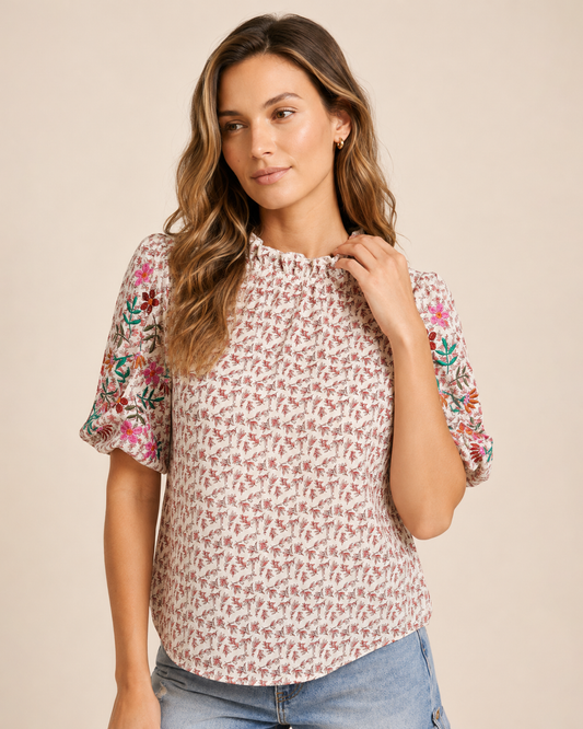 Close-up of a woman wearing a pink patchwork print short-sleeve top and light wash denim shorts on a beige background