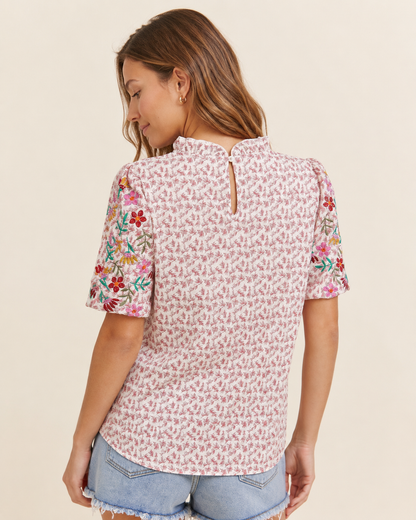 Back view of a woman wearing a pink patchwork print short-sleeve top and light wash denim shorts on a beige background