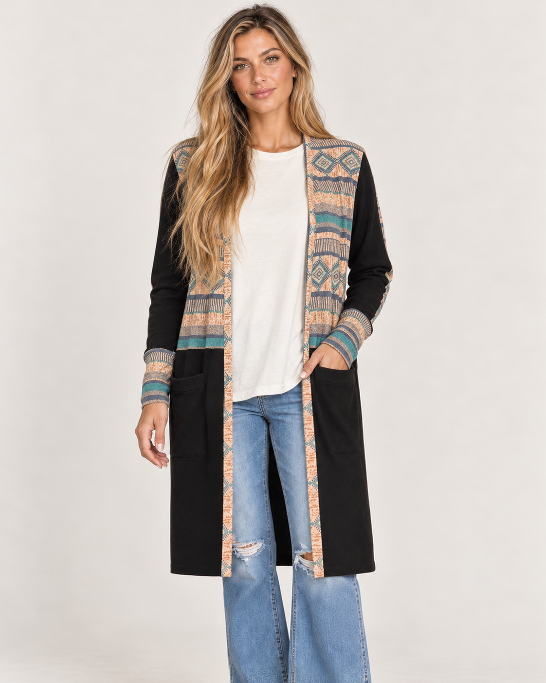 Full-body front view of a woman wearing a long black maxi cardigan with multicolor geometric patterned trim, a white top, and black wide-leg pants on a beige background.
