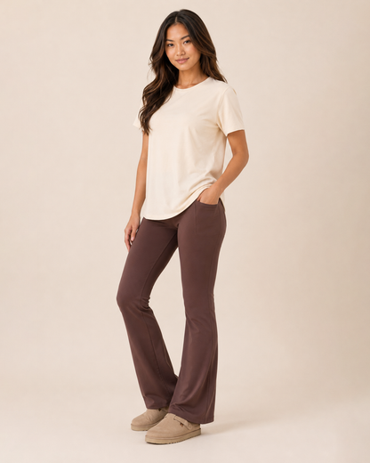 Full-body view of a woman wearing a cream graphic tee with brown pants and beige flats on a beige background