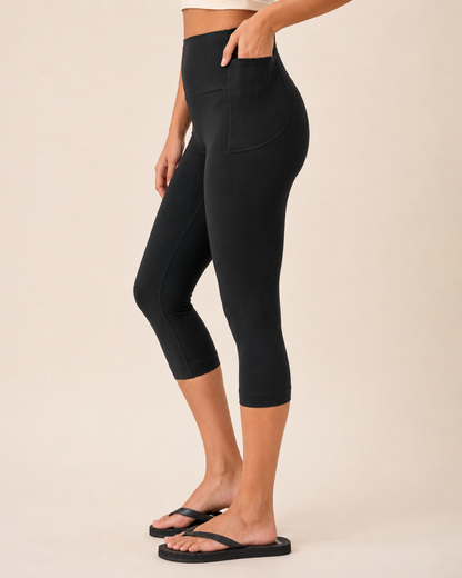 Side view of a woman wearing black capri leggings with a white top and black sandals on a beige background