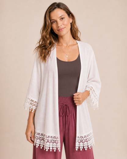 Woman wearing an ivory lace trim kimono over a dark brown dress with matching boots on a beige background