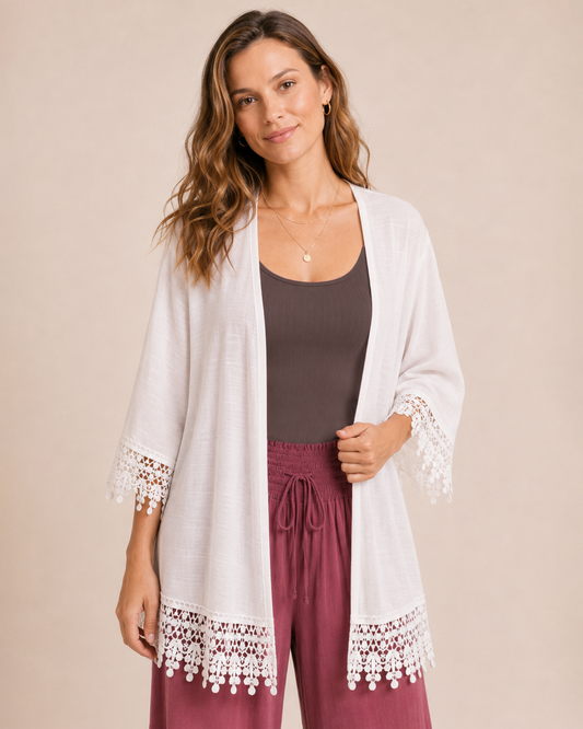 Woman wearing an ivory lace trim kimono over a dark brown dress with matching boots on a beige background