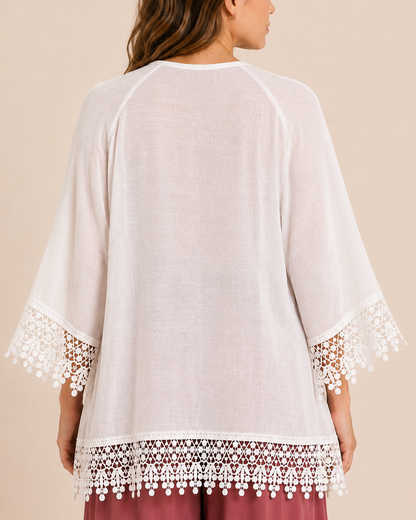 Back view of a woman wearing an ivory kimono with crochet lace trim along the sleeves and hem on a beige background