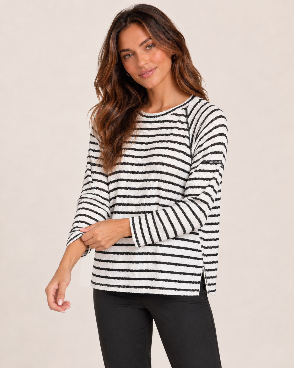 Cropped front view of a woman wearing a black and white striped long-sleeve pullover with black pants on a beige background