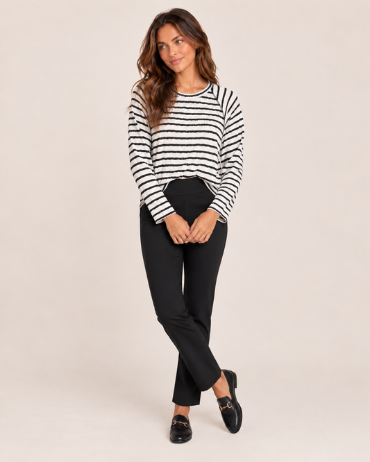 Cropped front view of a woman wearing a black and white striped long-sleeve pullover with black pants on a beige background
