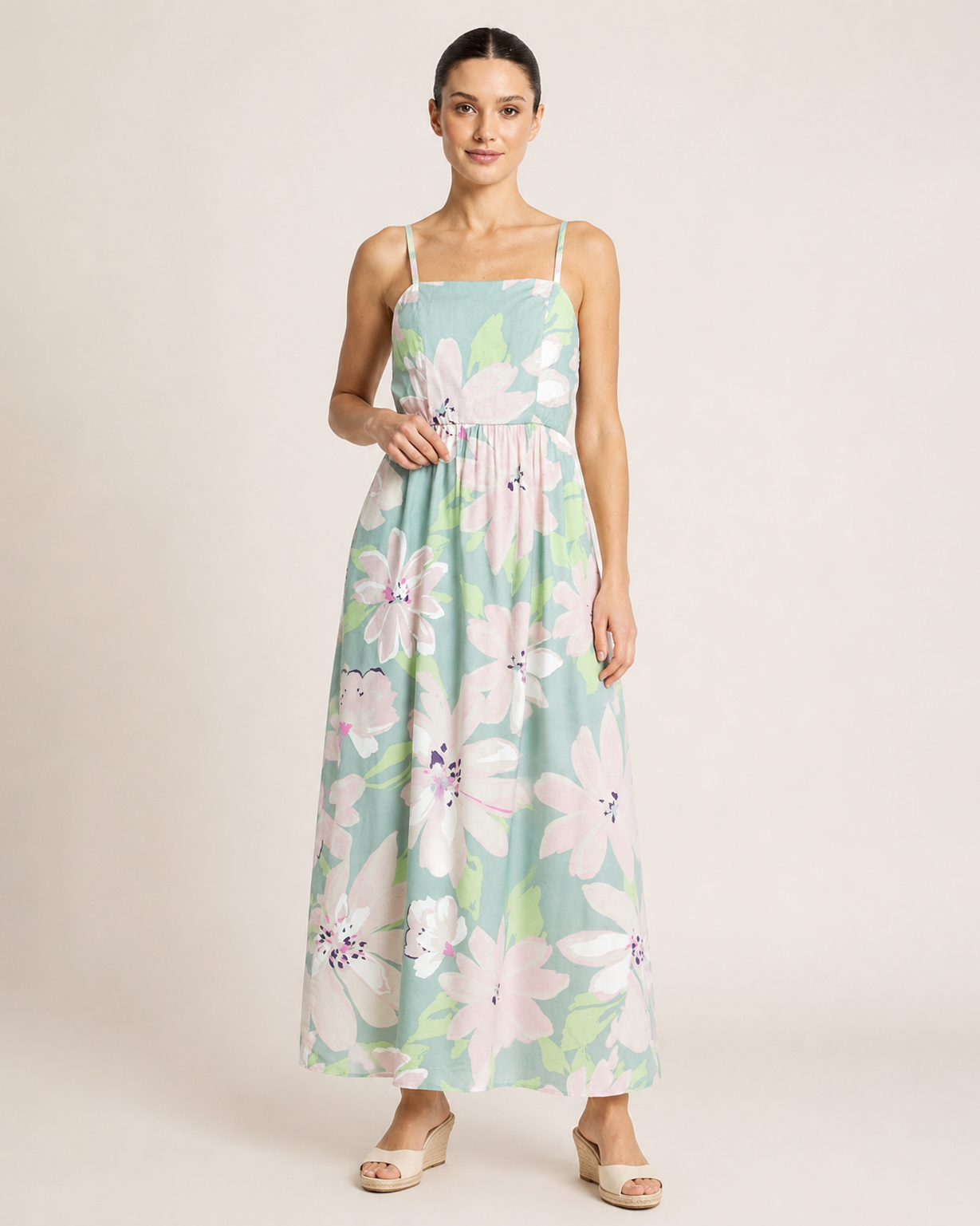 Full-body view of a woman wearing a pastel floral maxi dress and beige sandals on a beige background