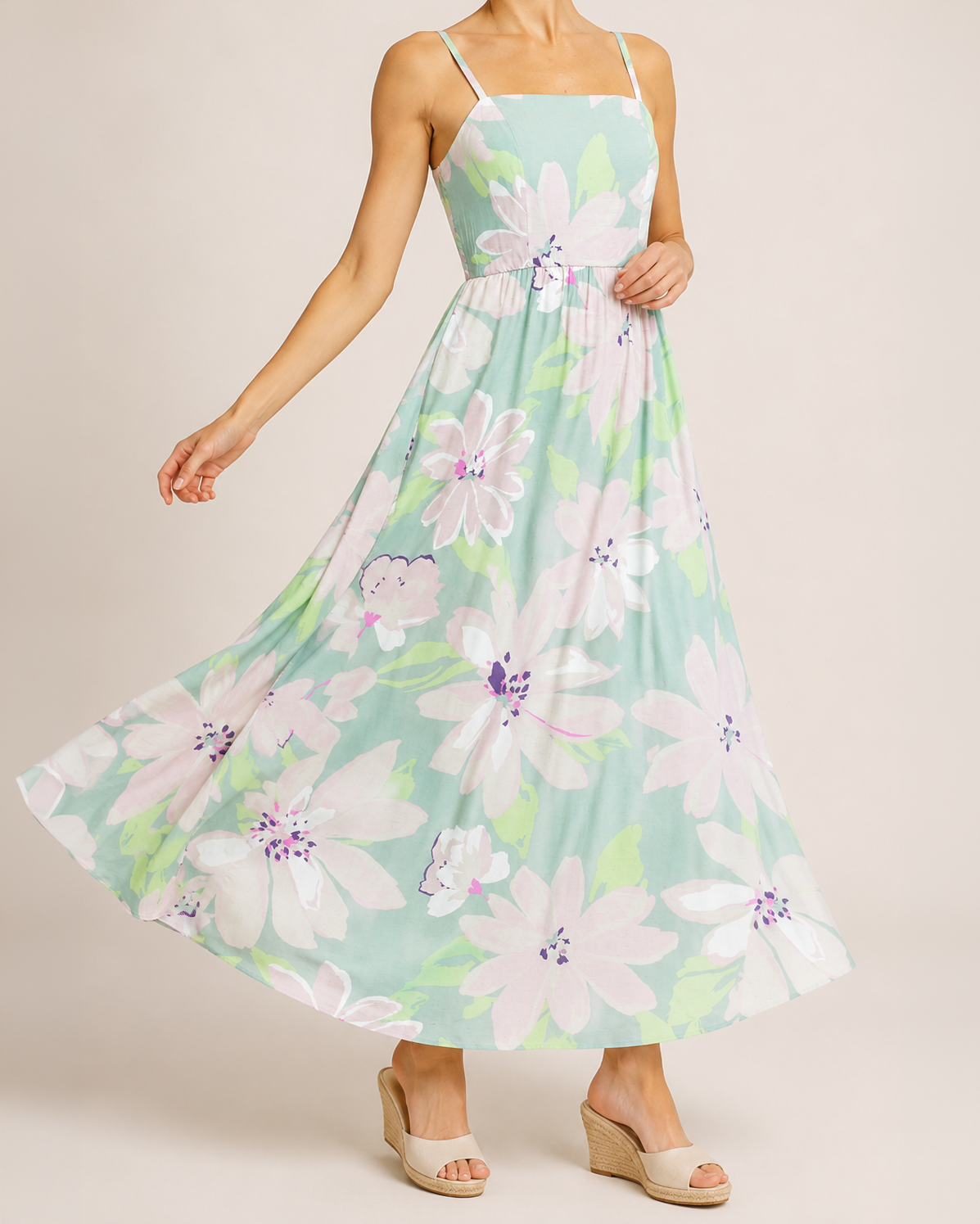 Front view of a woman wearing a pastel floral maxi dress and beige sandals on a beige background