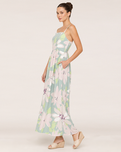 Walking view of a woman wearing a pastel floral maxi dress and beige sandals on a beige background