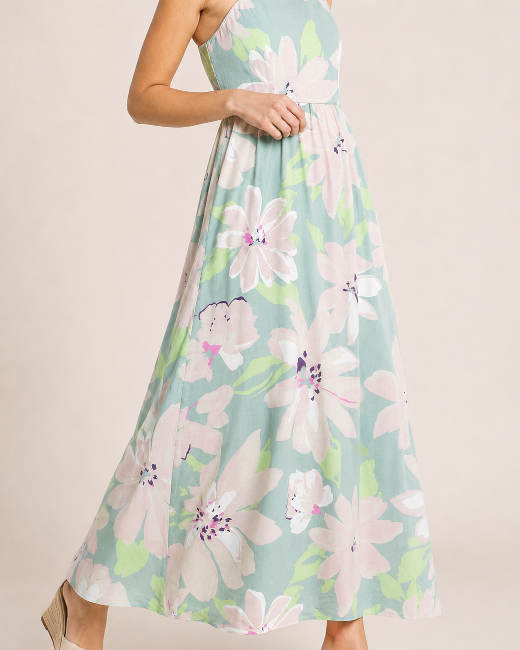Side view of a woman wearing a pastel floral maxi dress and beige sandals on a beige background