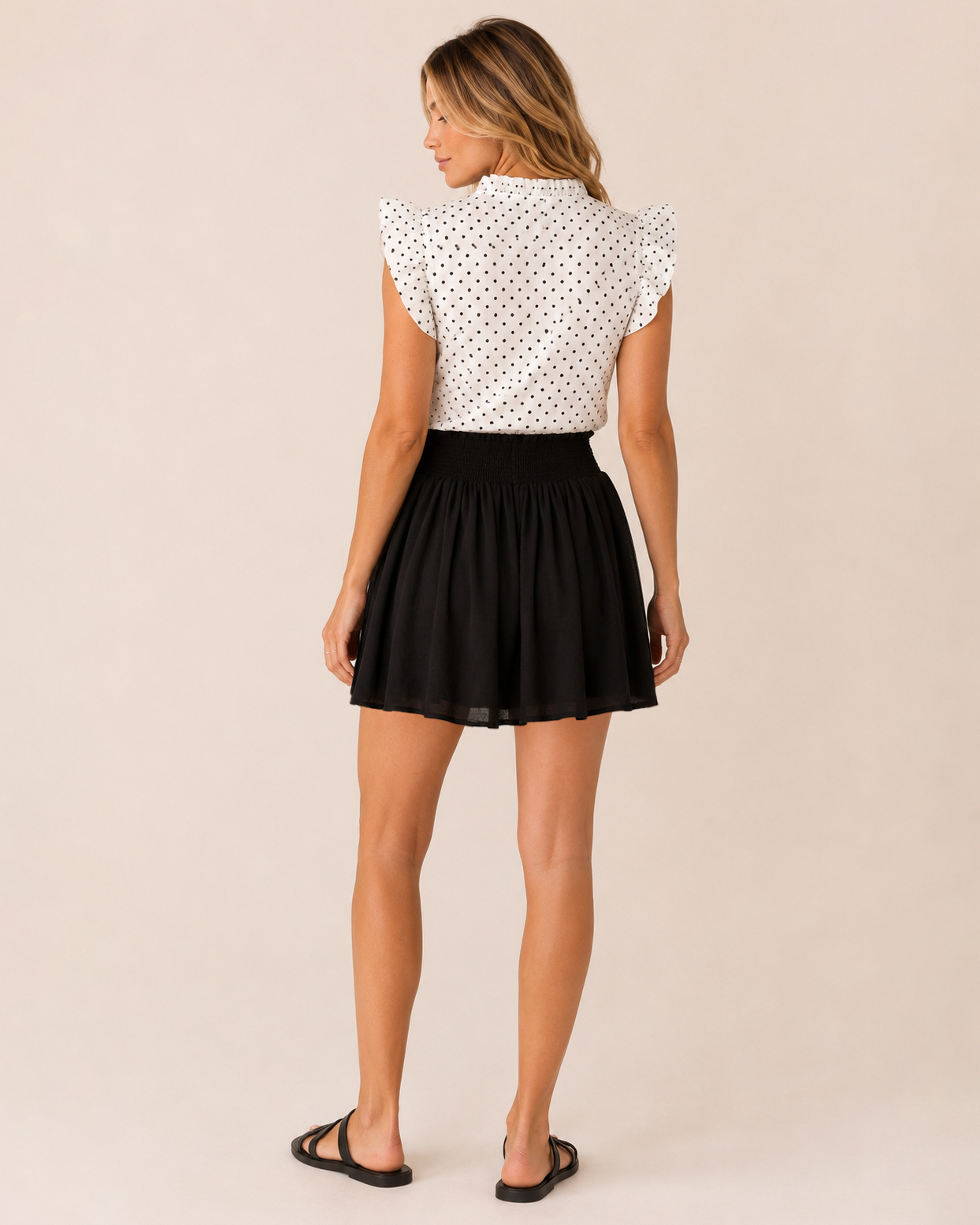 Back view of a woman wearing a black smocked waist skort and a white sleeveless top on a beige background