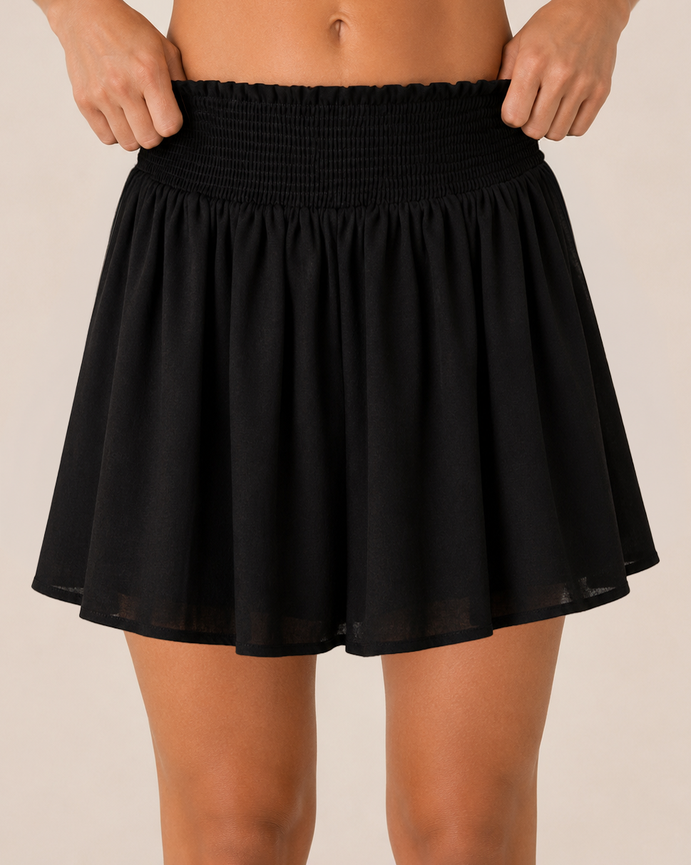 Close-up front view of a black smocked waist skort on a beige background