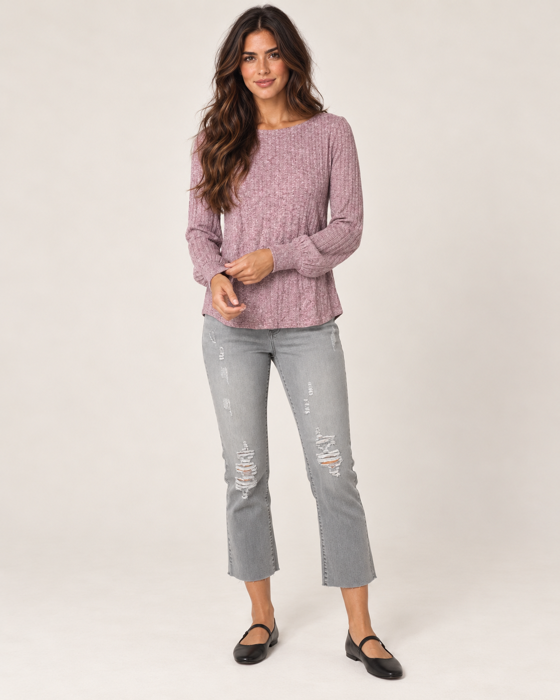Full-body front view of a woman wearing a dusty mauve lightweight crewneck sweater with gray jeans and taupe ankle boots on a beige background.