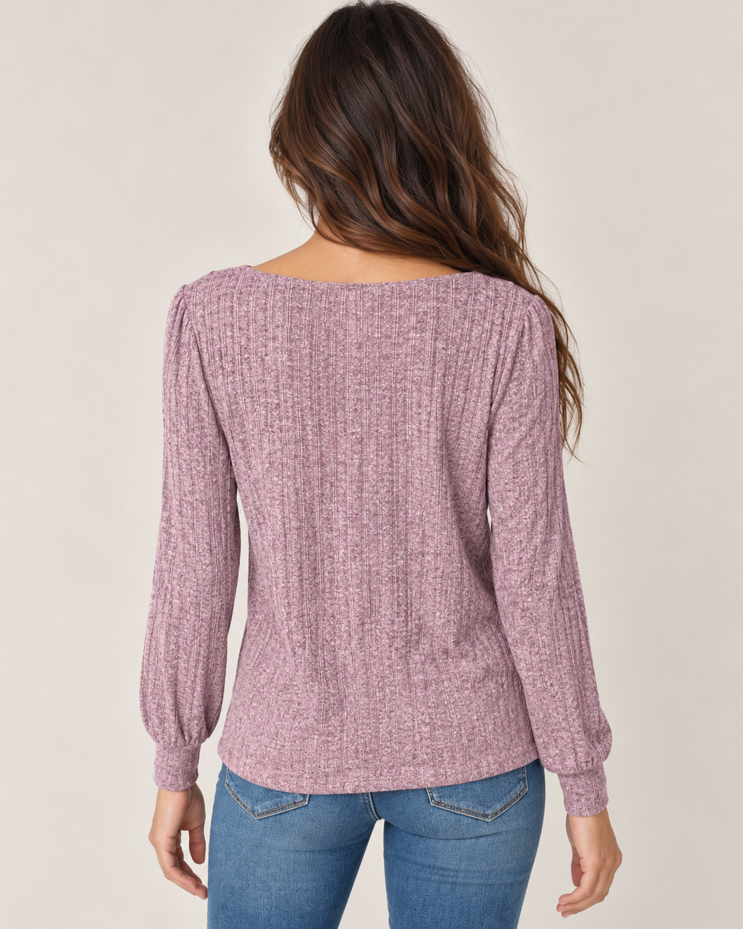 Back view of a woman wearing a dusty mauve lightweight crewneck sweater with long sleeves and blue jeans on a beige background.